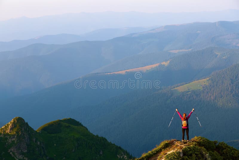 The tourist girl with the tracking sticks and the back sack at the edge of the cliff. The landscape with the high mountains. royalty free stock photography The tourist girl with the tracking sticks and the back sack at the edge of the cliff. The landscape with the high mountains. royalty free stock photography