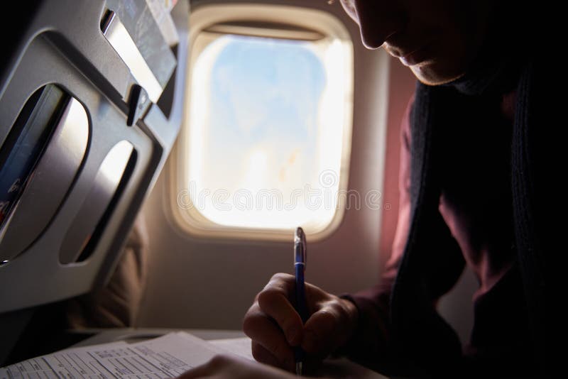 Tourist hand filling immigration form on flight to visit destination country sitting in airplane. Man is writing entry