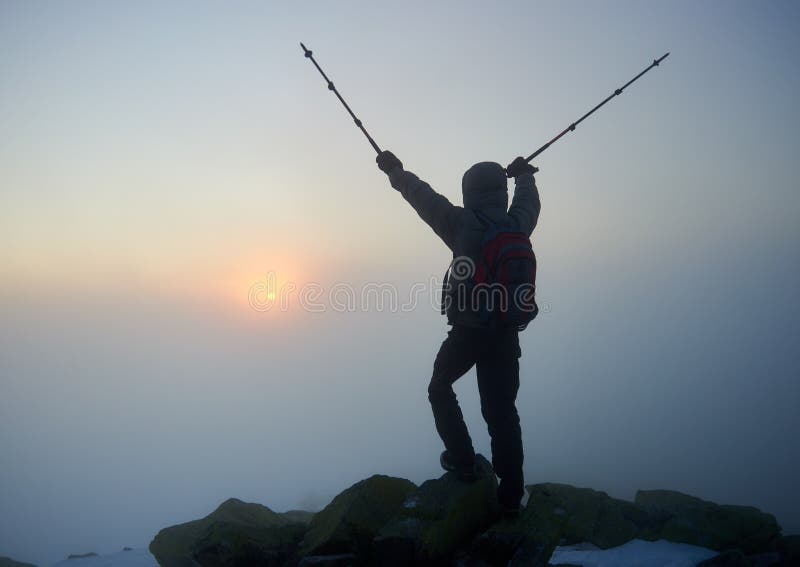 Tourist hiker man with backpack on rocky mountain on misty blue sky and raising sun background. royalty free stock photography Tourist hiker man with backpack on rocky mountain on misty blue sky and raising sun background. royalty free stock photography