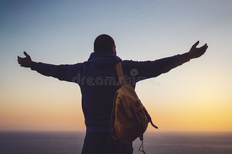 Tourist traveler with backpack standing with raised hands, hiker looking on sunset to valley in trip, hipster young man enjoying stock photo Tourist traveler with backpack standing with raised hands, hiker looking on sunset to valley in trip, hipster young man enjoying stock photo