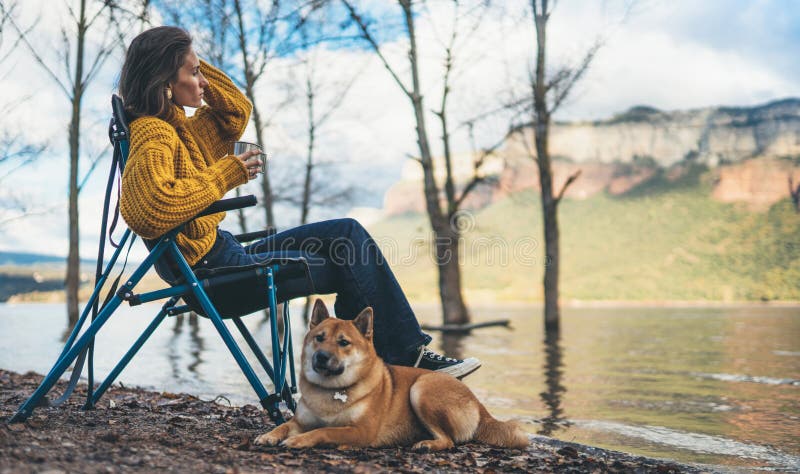 Tourist traveler girl drink tea leisure together dog on background mountain, puppy pet woman rest on lake shore nature trip, friendship concept