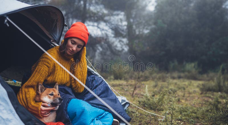 Tourist traveler hugging relaxation red shiba inu in camp tent on background foggy forest, hiker woman with puppy dog in mist nature trip, friendship love concept, copy space