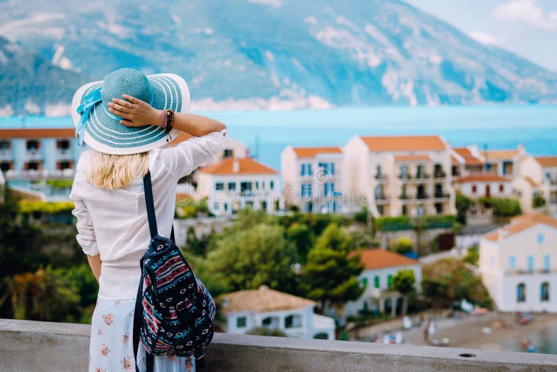 Tourist woman admiring view of colorful tranquil village Assos on morning. Young stylish female model wearing blue