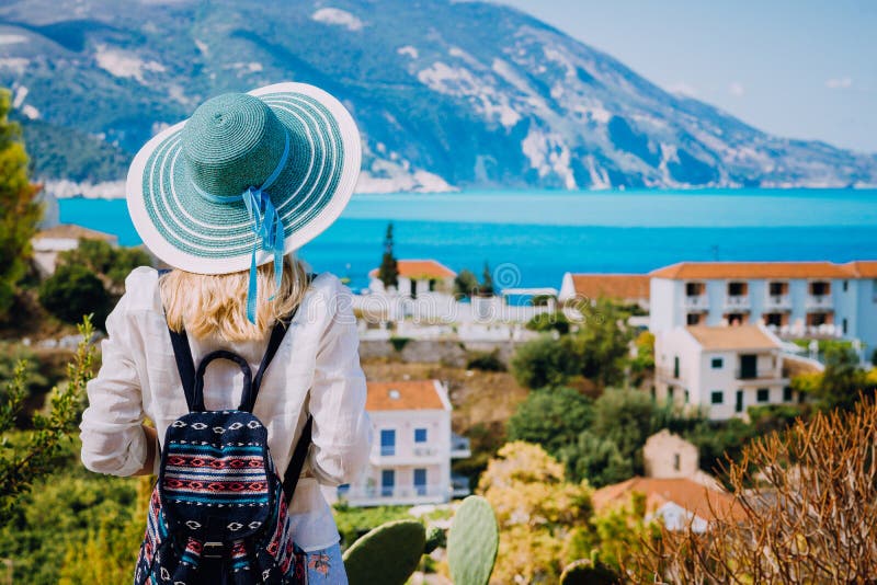 Tourist woman with blue sunhat and travel backpack admire view of colorful tranquil village Assos on sunny day. Visiting