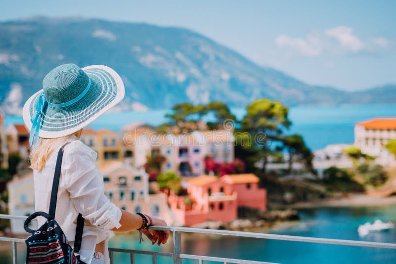 Tourist woman wearing blue sunhat and white clothes enjoying view of colorful tranquil village Assos on sunny day