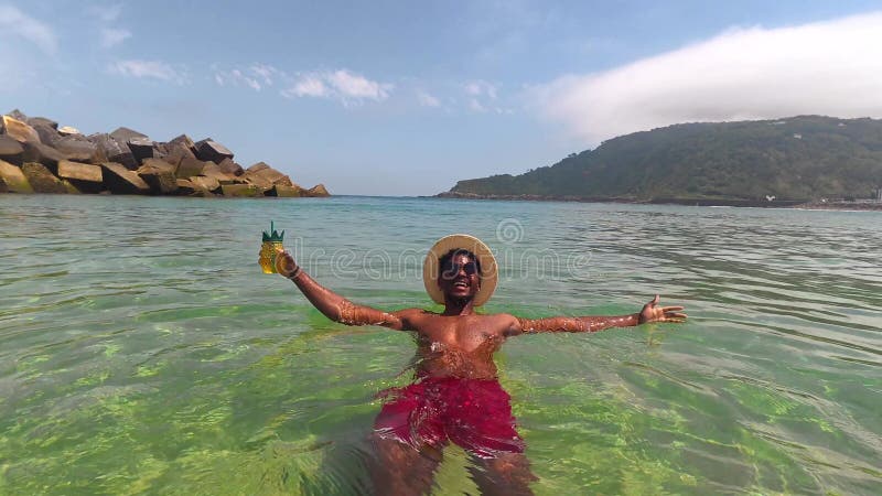 Touriste dégustant un cocktail d'ananas dans une eau cristalline de l'océan banque de vidéos