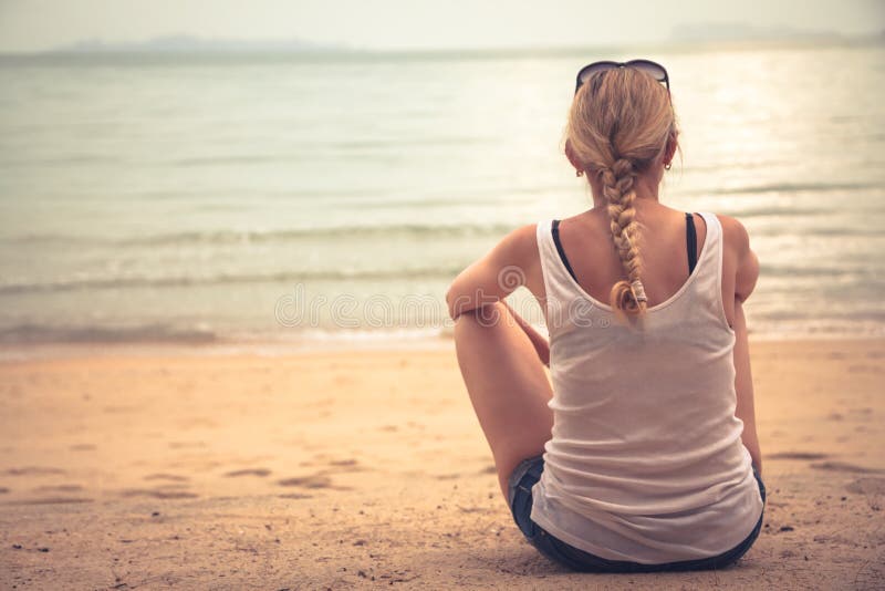 Touriste songeur de jeune femme s'asseyant sur la plage et examinant la distance photo stock Touriste songeur de jeune femme s'asseyant sur la plage et examinant la distance photo stock