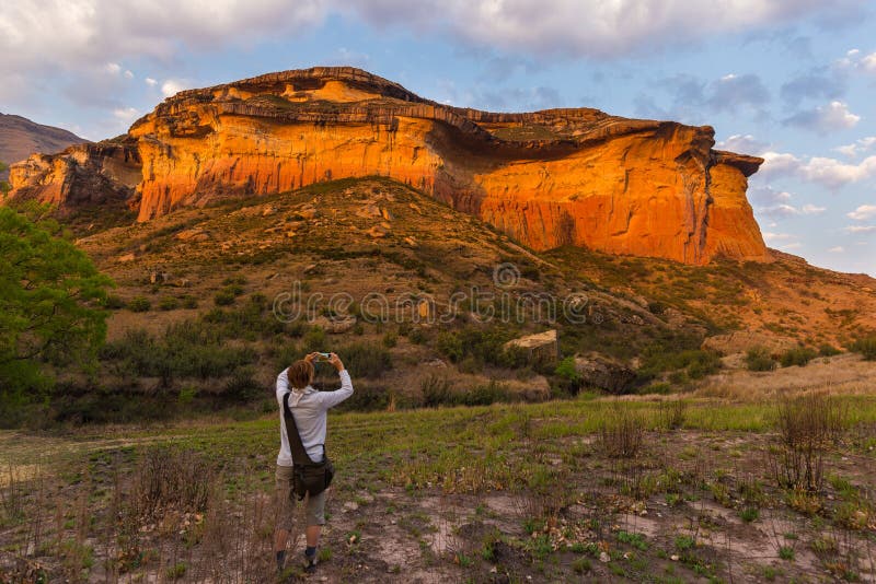 Touriste tenant le téléphone intelligent et prenant la photo à la falaise scénique illuminée par la lumière de coucher du soleil image stock Touriste tenant le téléphone intelligent et prenant la photo à la falaise scénique illuminée par la lumière de coucher du soleil image stock