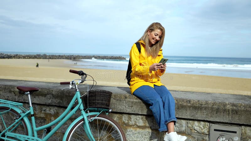 Touriste utilisant smartphone tout en se reposant sur le mur de plage avec vélo banque de vidéos