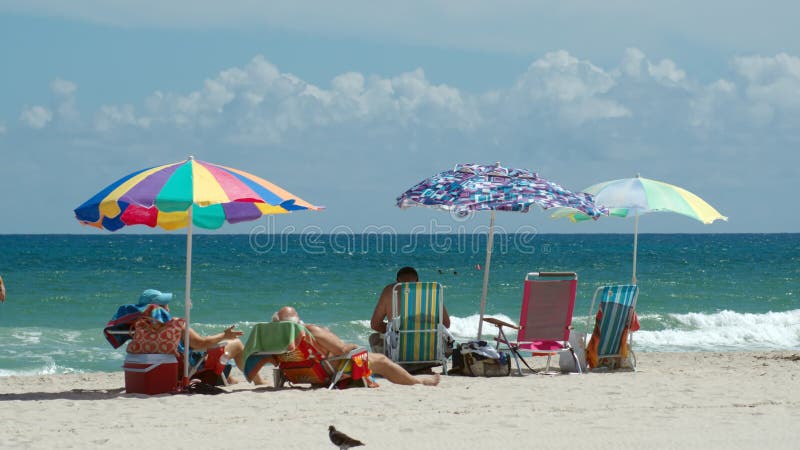 Tourists under colorful beach umbrellas by the ocean, on Dania Beach in Fort Lauderdale, Florida, USA. Tourists under colorful beach umbrellas by the ocean, on Dania Beach in Fort Lauderdale, Florida, USA