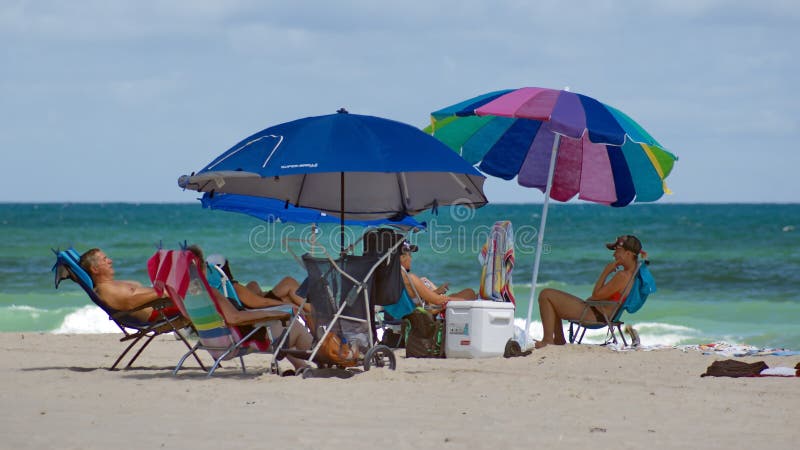 Tourists under colorful beach umbrellas by the ocean, on Dania Beach in Fort Lauderdale, Florida, USA. Tourists under colorful beach umbrellas by the ocean, on Dania Beach in Fort Lauderdale, Florida, USA