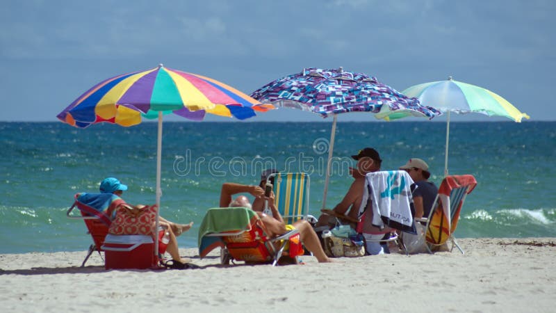 Tourists under colorful beach umbrellas by the ocean, on Dania Beach in Fort Lauderdale, Florida, USA. Tourists under colorful beach umbrellas by the ocean, on Dania Beach in Fort Lauderdale, Florida, USA