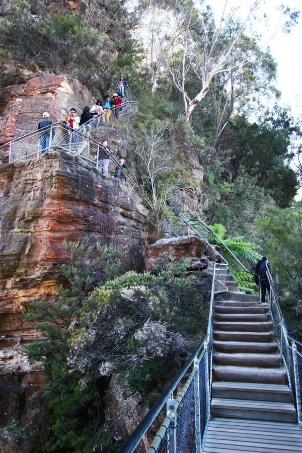 Touristes trimardant à la traînée raide de zigzag de l'escalier grand le long de la falaise rouge de cisaillement de roche avec l images libres de droits Touristes trimardant à la traînée raide de zigzag de l'escalier grand le long de la falaise rouge de cisaillement de roche avec l images libres de droits