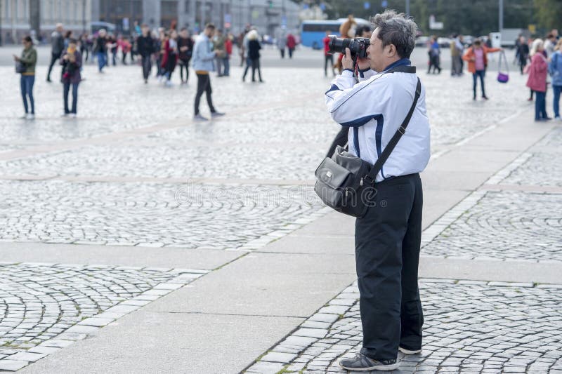 Touristische asiatische Auftrittphotographien des Mannes auf Kameraanziehungskräften auf dem Palastquadrat von St Petersburg, Rus stockfoto Touristische asiatische Auftrittphotographien des Mannes auf Kameraanziehungskräften auf dem Palastquadrat von St Petersburg, Rus stockfoto