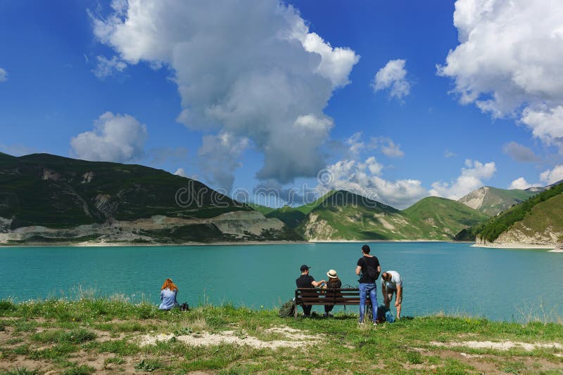 Tourists sit on a bench on the shore of lake Kezenoi am. Green grass on the mountain slopes in early summer stock photo Tourists sit on a bench on the shore of lake Kezenoi am. Green grass on the mountain slopes in early summer stock photo