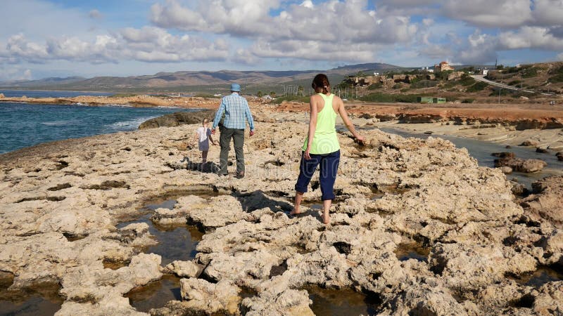 Tourists walk along the sharp loose limestone coast along the sea.