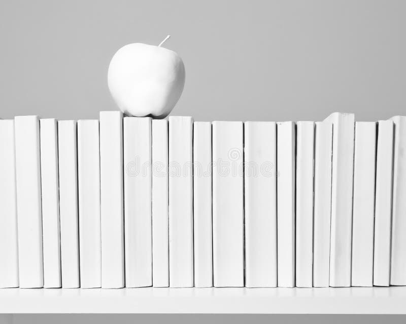 A row of all white books sit on a white shelf with a white apple in front of an off white background. A row of all white books sit on a white shelf with a white apple in front of an off white background.