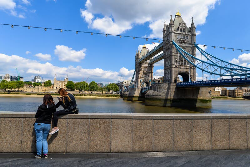 5/25/19 - People sitting on the ledge next to the River thames and iconic landmarks in London - London, UK. 5/25/19 - People sitting on the ledge next to the River thames and iconic landmarks in London - London, UK