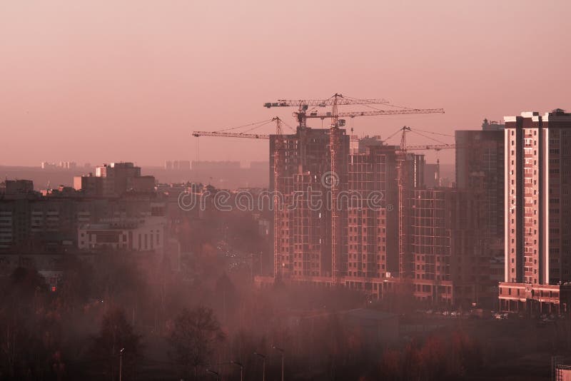 Tower cranes, the construction of a new tall apartment building at a construction site in the city at sunset or sunrise. Profitabl