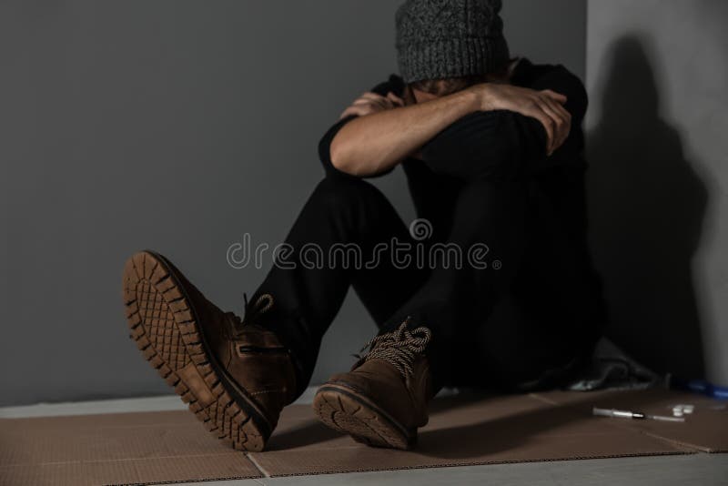 Stoned drug addict sitting on floor near grey wall. Stoned drug addict sitting on floor near grey wall