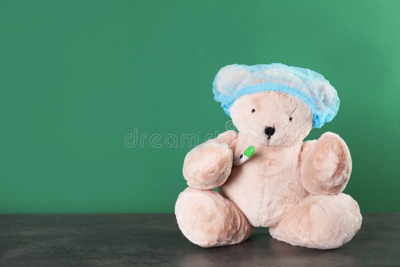 Toy bear with thermometer on table against color background. Children`s hospital