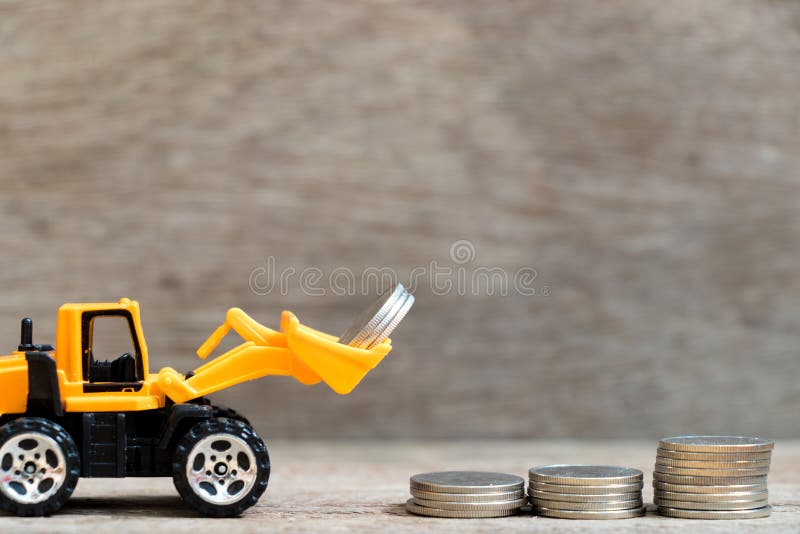 Toy bulldozer hold group of coin to fulfill up trend of stacked coin on wood background