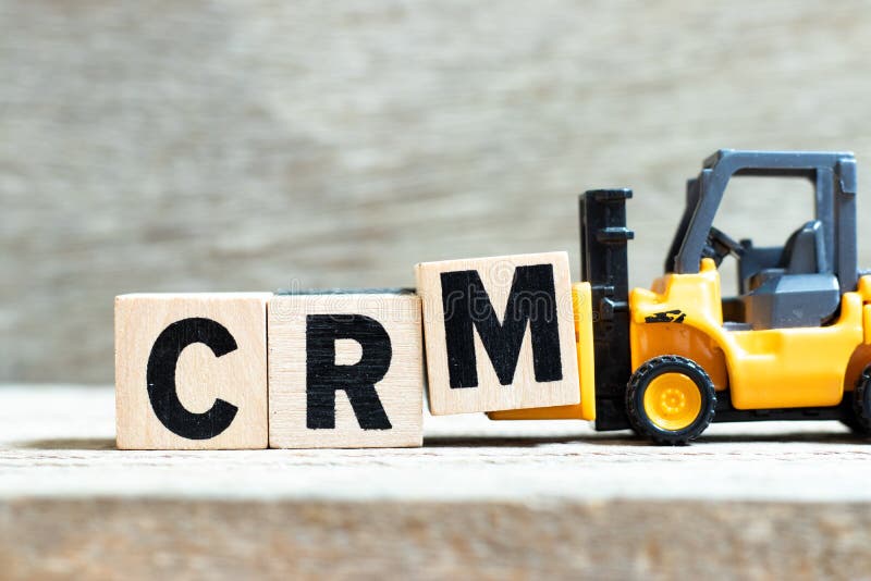 Toy forklift hold letter block M to complete word CRM Abbreviation of Customer Relationship Management on wood background
