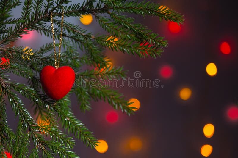 Toy in the shape of a red heart on the background of glowing lights. Christmas card, background. There is a place for text.