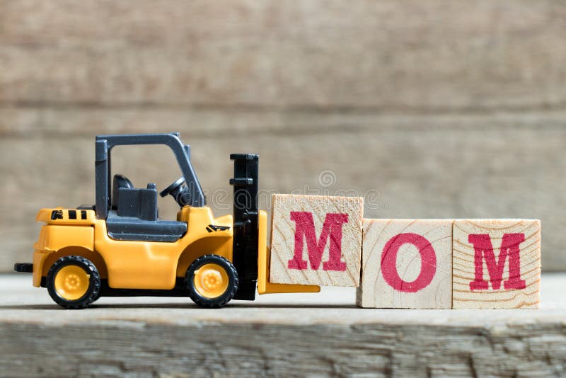 Toy yellow forklift hold letter block M to complete word mom on wood background &#x28;Concept for mother &#x27;s day