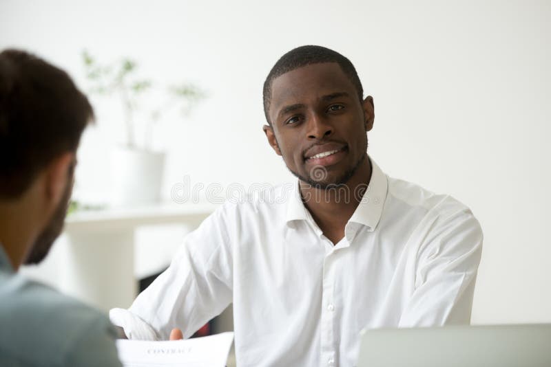 Trabajador afroamericano sonriente que mira la cámara en oficina imagenes de archivo Trabajador afroamericano sonriente que mira la cámara en oficina imagenes de archivo