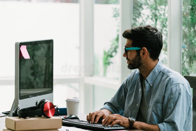 Trabajador caucásico con barba y bigote en camisa informal usando computadora de escritorio en casa