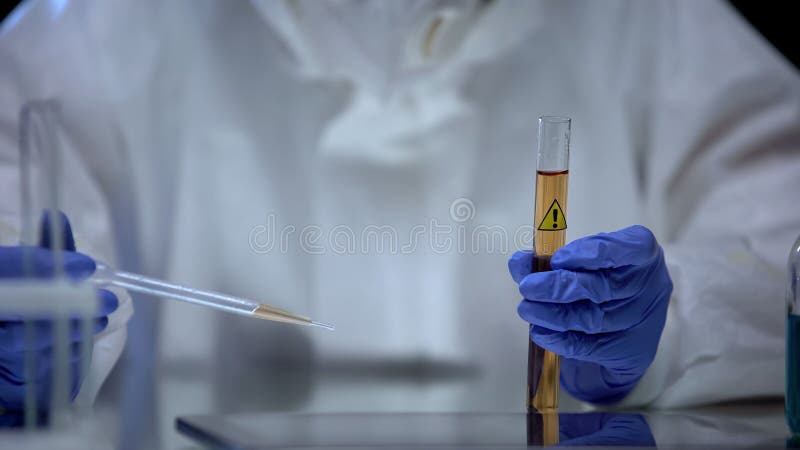 Trabajador de laboratorio de química estudiando una muestra de detergente del tubo con signo de precaución fotos de archivo Trabajador de laboratorio de química estudiando una muestra de detergente del tubo con signo de precaución fotos de archivo