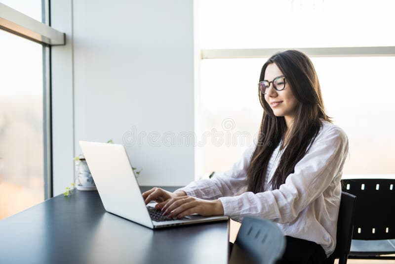 Trabajador de mujer que se sienta en oficina mientras que usa el ordenador portátil y mecanografía por el teclado imagen de archivo