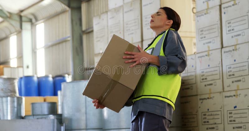 Trabajador de sexo femenino que sufre de dolor de espalda mientras que sostiene la caja pesada 4k