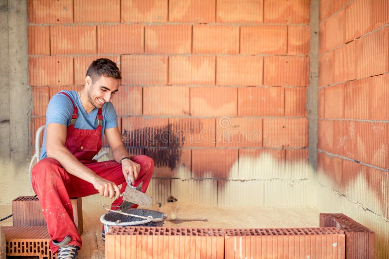 Trabajador del albañil de la construcción, paredes de ladrillo del edificio del albañil con la espátula y mortero fotografía de archivo