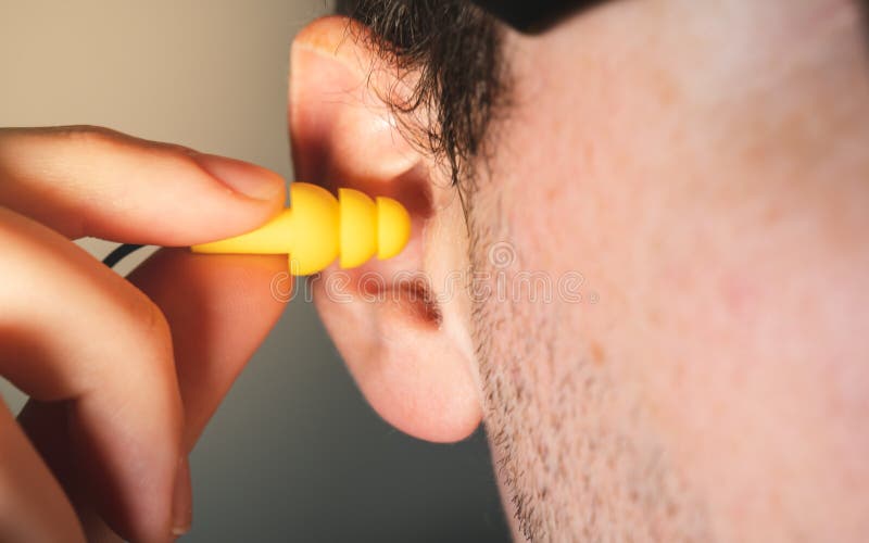 Trabajador del hombre que inserta el auricular amarillo de la protección de la seguridad de la audición en su cierre del oído enc foto de archivo libre de regalías Trabajador del hombre que inserta el auricular amarillo de la protección de la seguridad de la audición en su cierre del oído enc foto de archivo libre de regalías
