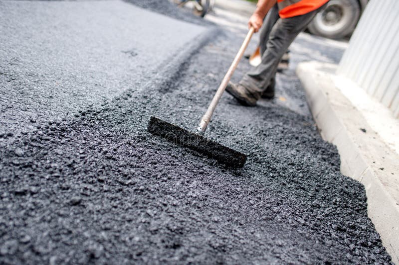 Trabajador que nivela el asfalto fresco en un sitio de la construcción de carreteras
