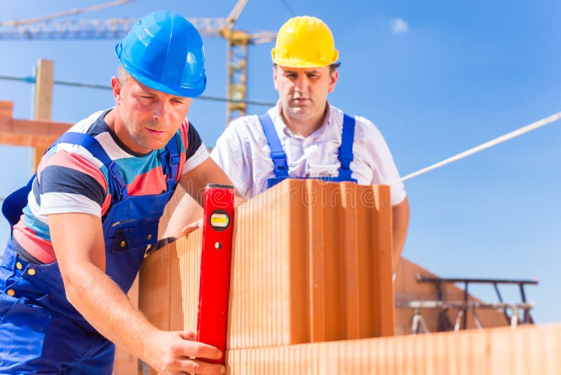 Construction site workers or bricklayer with helmets controlling building walls with a bubble level. Construction site workers or bricklayer with helmets controlling building walls with a bubble level