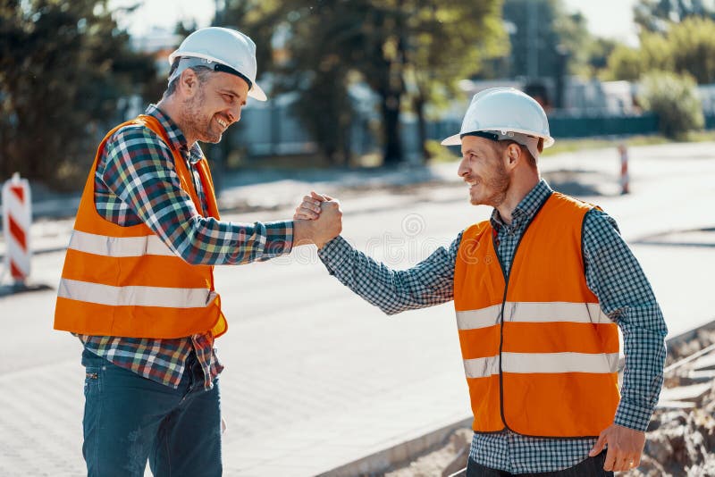 Trabajadores sonrientes en chalecos reflexivos y cascos blancos que saludan e fotografía de archivo libre de regalías Trabajadores sonrientes en chalecos reflexivos y cascos blancos que saludan e fotografía de archivo libre de regalías