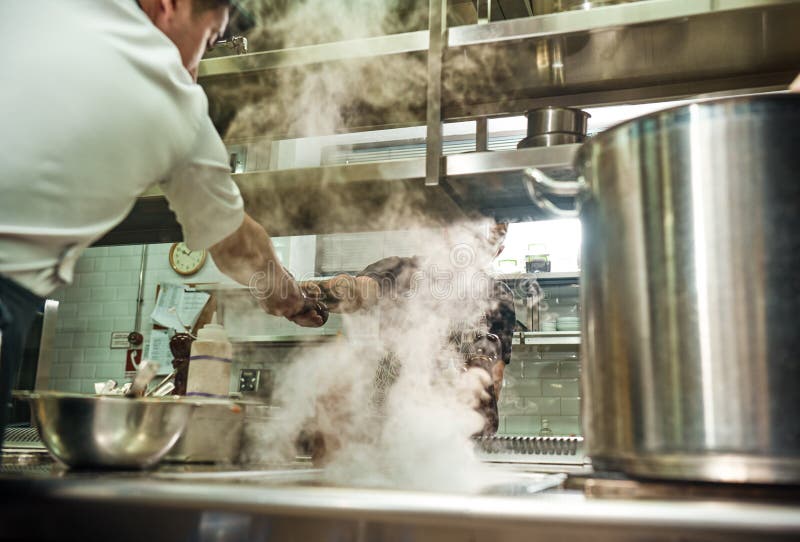 Trabajo en equipo Cocinero del restaurante que da una amoladora de pimienta a su ayudante mientras que proceso de cocinar en la c fotos de archivo libres de regalías Trabajo en equipo Cocinero del restaurante que da una amoladora de pimienta a su ayudante mientras que proceso de cocinar en la c fotos de archivo libres de regalías