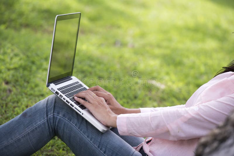 Trabajo hermoso joven de la mujer al aire libre en un parque p? blico Trabajo en la computadora port? til al aire libre Imagen cose. Young beautiful woman working outdoor in a public park. Working on laptop outdoors. Cropped image of female working on laptop while sitting in a park