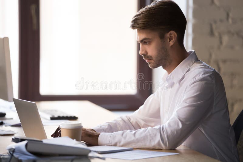 Trabajo ocupado enfocado del empleado de sexo masculino en el ordenador portátil en oficina foto de archivo libre de regalías Trabajo ocupado enfocado del empleado de sexo masculino en el ordenador portátil en oficina foto de archivo libre de regalías