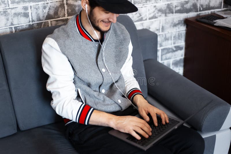 Trabajo sonriente del hombre joven en el ordenador portátil en el sofá imagen de archivo libre de regalías Trabajo sonriente del hombre joven en el ordenador portátil en el sofá imagen de archivo libre de regalías