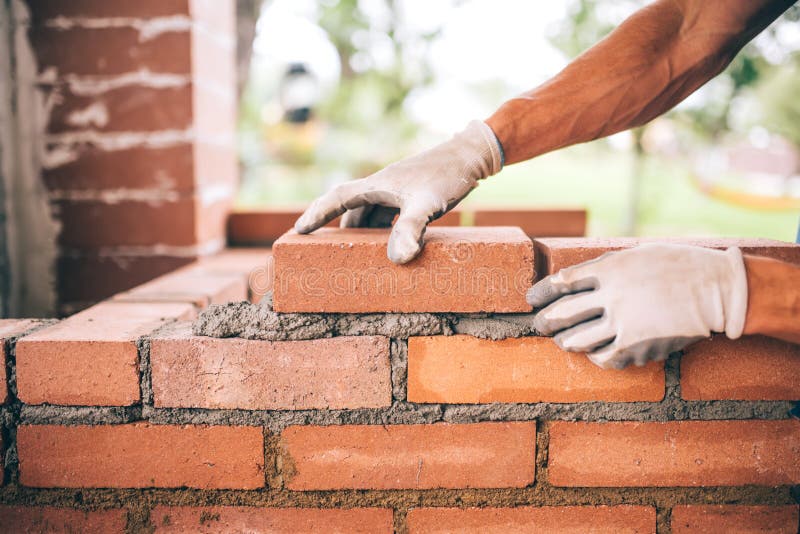 trabalhador da construção que coloca tijolos e que constrói o assado no local industrial Detalhe de mão que ajusta tijolos