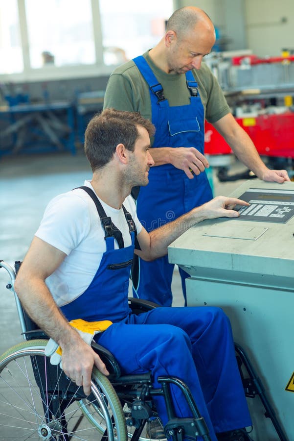 Trabalhador deficiente na cadeira de rodas na fábrica e no colega