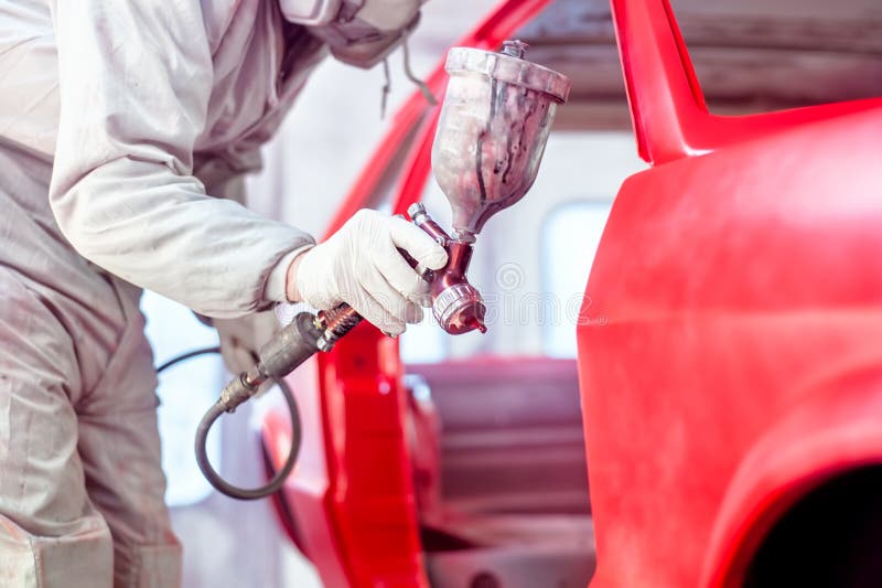 Trabalhador profissional que pulveriza a pintura vermelha em um corpo de carro