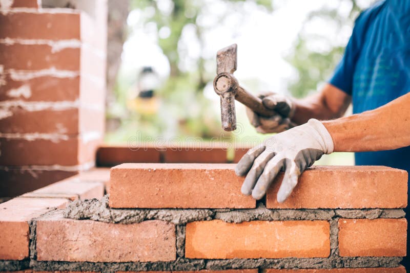 Trabalhador que constrói paredes exteriores, usando o martelo para colocar tijolos no cimento Detalhe de trabalhador com ferramen