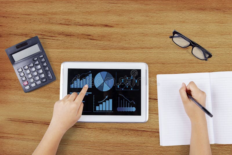 Closeup of businessperson hands analyzing business charts with digital tablet while writing on the book. Closeup of businessperson hands analyzing business charts with digital tablet while writing on the book