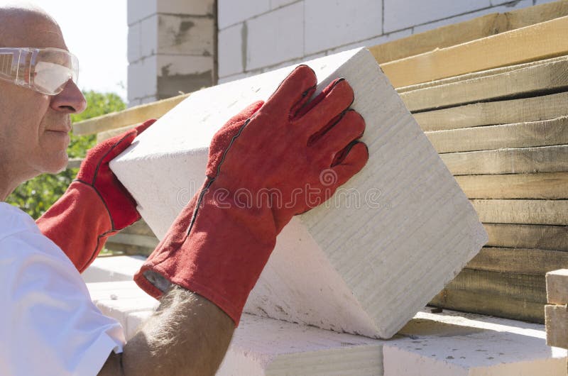 Trabalhador usando luvas protetoras e tomando tijolo branco Processo de construção de uma casa fotografia de stock royalty free Trabalhador usando luvas protetoras e tomando tijolo branco Processo de construção de uma casa fotografia de stock royalty free