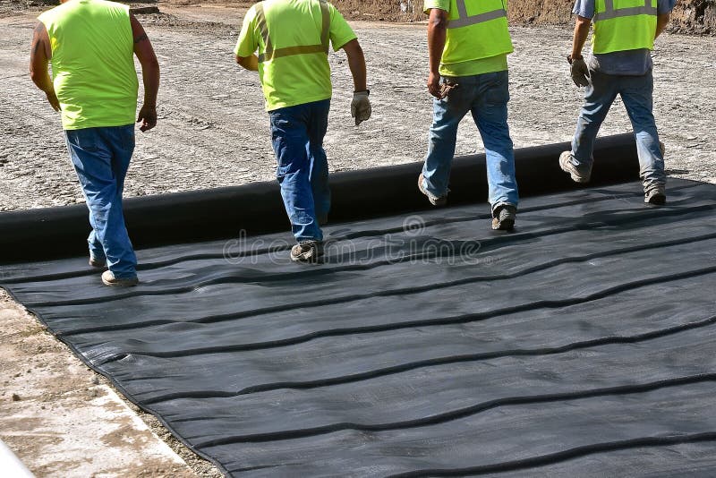 Vested construction workers unroll a layer of tarpaulin  in a road construction project. Vested construction workers unroll a layer of tarpaulin  in a road construction project